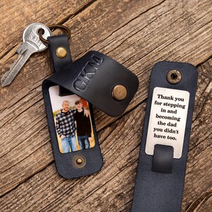 May include: A dark blue leather keychain with a metal snap closure, featuring the embossed letters GKM, a photograph of two people, and a metal tag engraved with the text: Thank you for stepping in and becoming the dad you didn't have too.