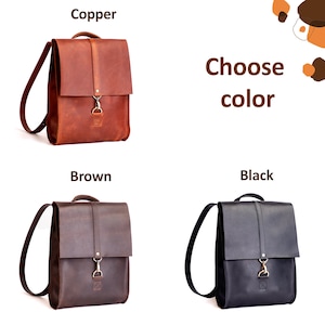 May include: Three backpacks in copper, brown, and black colors. Each backpack features a top flap with a vertical strap, a metal clasp closure, a top handle, and shoulder straps. The text "Choose color" is displayed with labels for each option.