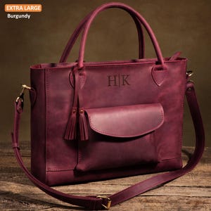 May include: An extra large burgundy leather tote bag featuring two top handles, a detachable shoulder strap, and a front pocket with a flap. The bag is embossed with the letters H|K and includes decorative leather tassels on one side.