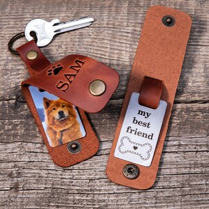 May include: A brown leather keychain with a metal snap closure, featuring a photo of a dog and the name SAM engraved with a paw print. Beside it, a matching leather strap displays a metal tag with the text my best friend and a bone icon.