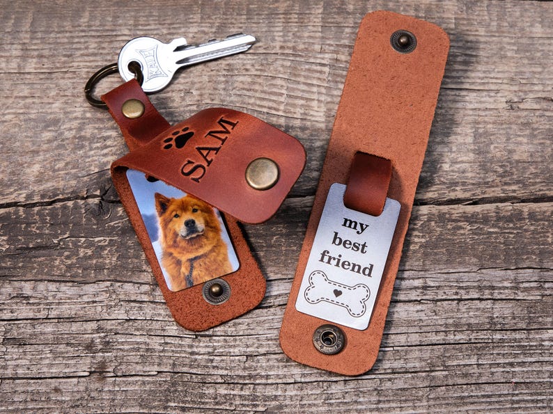 May include: A brown leather keychain with a metal snap closure, featuring a photo of a dog and the name SAM engraved with a paw print. Beside it, a matching leather strap displays a metal tag with the text my best friend and a bone icon.