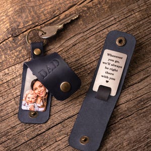 May include: A dark blue leather keychain with a metal key ring and a metal key. The leather flap is embossed with the word DAD and features a photo of a woman and a baby. A second leather piece displays the engraved text: Wherever you go, we'll always be right there with you.
