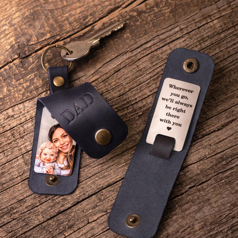 May include: A dark blue leather keychain with a metal key ring and a metal key. The leather flap is embossed with the word DAD and features a photo of a woman and a baby. A second leather piece displays the engraved text: Wherever you go, we'll always be right there with you.