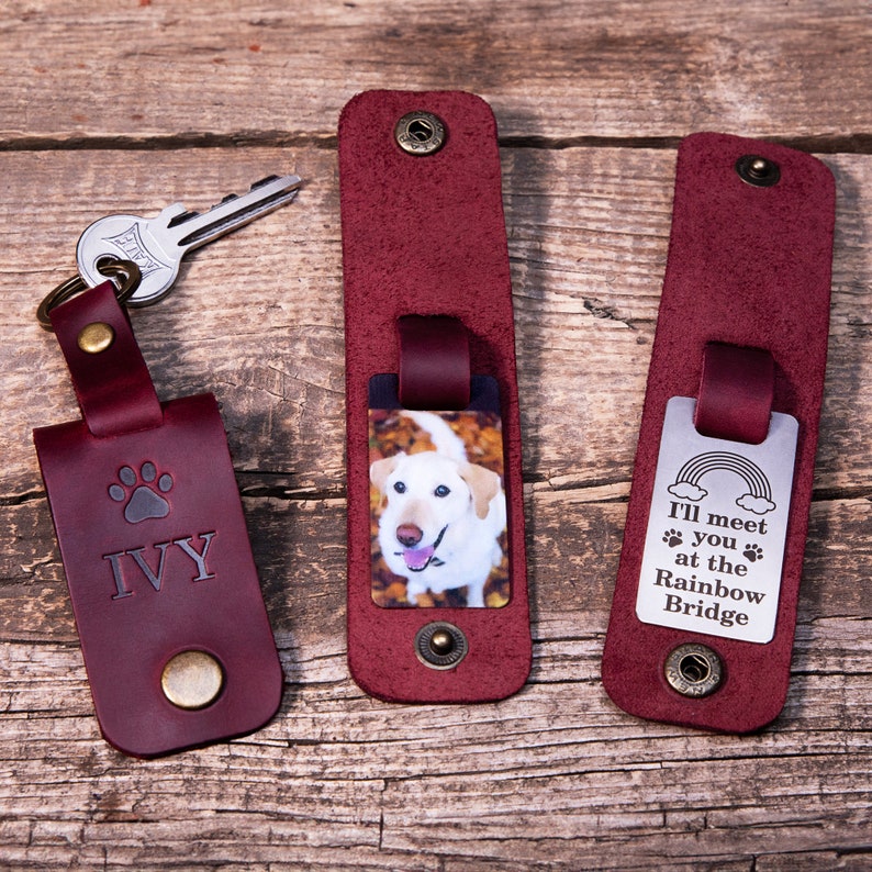 May include: Three burgundy leather key fobs with metal snap closures. One features a paw print and the name IVY, one displays a photo of a white dog, and one shows a rainbow graphic with the text I'll meet you at the Rainbow Bridge.