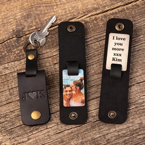 May include: Three black leather keychains with brass-colored snap buttons. One keychain holds a metal key and features the letters J and K with a heart. Another displays a color photograph of a couple. The third shows the text I love you more xxx Kim.