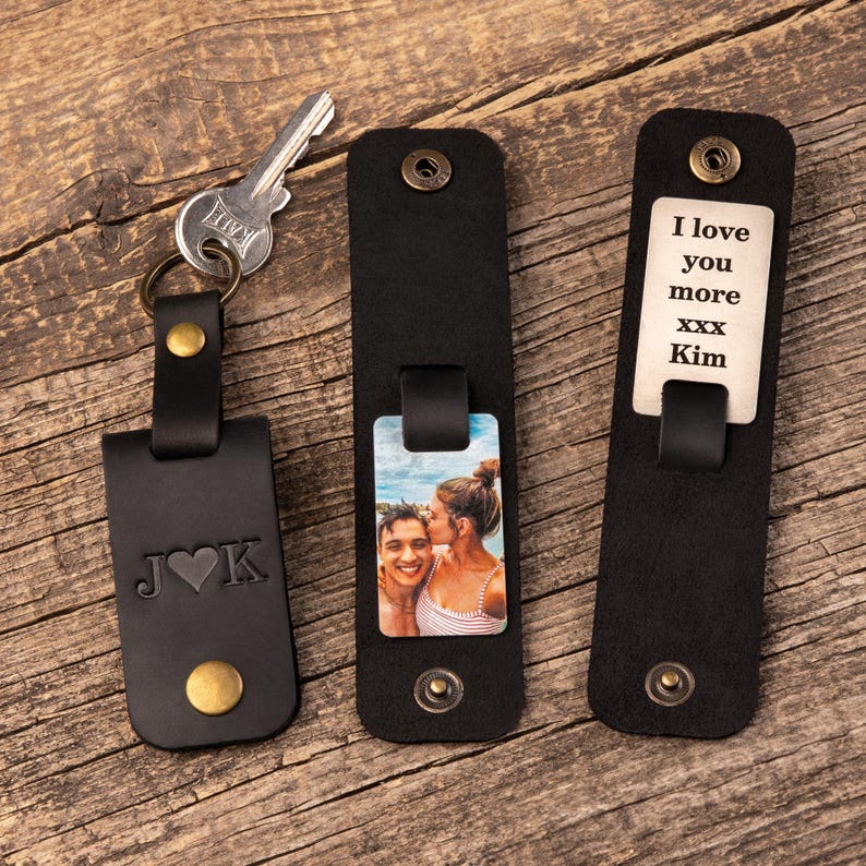 May include: Three black leather keychains with brass-colored snap buttons. One keychain holds a metal key and features the letters J and K with a heart. Another displays a color photograph of a couple. The third shows the text I love you more xxx Kim.