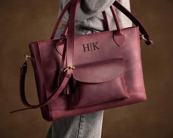 May include: A deep burgundy leather tote bag featuring two top handles, an adjustable shoulder strap, and a front pocket with a flap closure. The bag is embossed with the letters H|K in the center and includes a decorative leather tassel detail.
