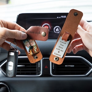 May include: Two brown leather keychains with metal snaps. One keychain features a photo of two people and the text Drive safe. The other keychain features a metal tag engraved with the text I need You Here with me heart Lauren.