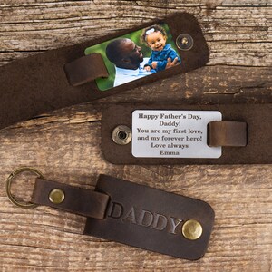 May include: Three dark brown leather keychains with brass-toned metal snaps. One keychain features a color photograph of a man and a child, another displays the engraved text: Happy Father's Day, Daddy! You are my first love, and my forever hero! Love always Emma, and the third is embossed with the word DADDY.