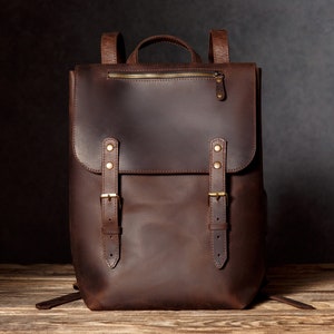 May include: A brown leather backpack with two adjustable straps and a zip closure. The backpack has brass buckles and hardware.