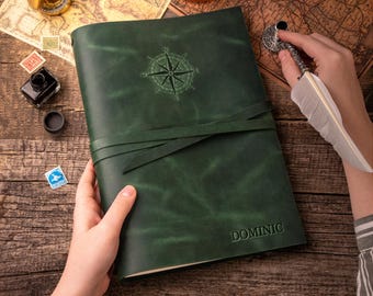 May include: A dark green leather journal featuring a debossed compass rose on the front cover and the name DOMINIC embossed in the bottom right corner. The journal is secured with a matching leather wrap tie closure.