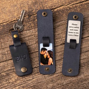 May include: Three dark blue leather keychains with brass hardware. One features the embossed letters E+C, one displays a color photograph of a couple, and one shows a metal tag engraved with the text: Please drive safely and come home to me. Love, Chloe.