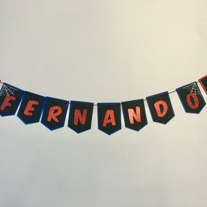 May include: A black and blue banner with the name "Fernando" spelled out in red glitter letters. The banner has a Spiderman character on each end.