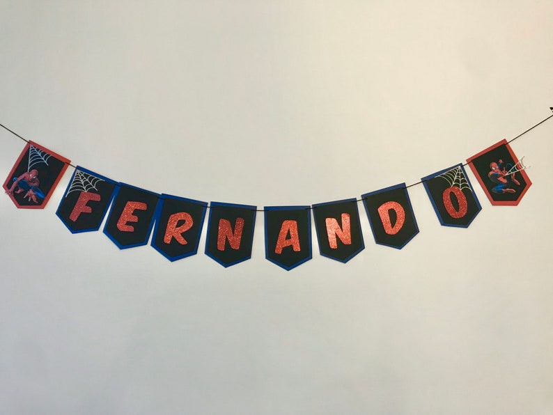 May include: A black and blue banner with the name "Fernando" spelled out in red glitter letters. The banner has a Spiderman character on each end.