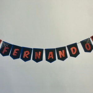 May include: A banner with the name "FERNANDO" spelled out in copper glitter letters on black pennants with blue trim. Each pennant has a small spider-man graphic.