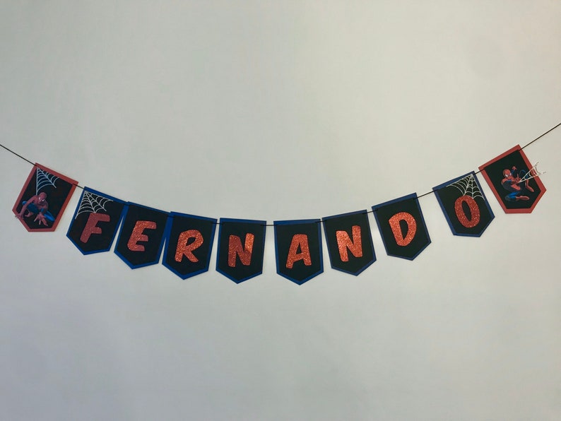 May include: A banner with the name "FERNANDO" spelled out in copper glitter letters on black pennants with blue trim. Each pennant has a small spider-man graphic.