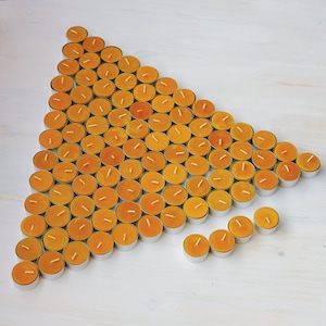 Puede incluir: Un gran grupo de pequeñas velas de té redondas amarillas dispuestas en forma triangular sobre una superficie blanca.