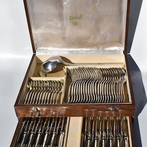 May include: A wooden storage chest containing a 61-piece silver flatware set for 12 people, featuring the Christofle brand name on the interior satin lining. The set includes various spoons, forks, and knives arranged in compartments.