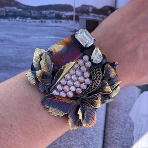 Può includere: Bracciale a polsino ornato con un design floreale nei toni del bronzo, oro e viola. Il bracciale è impreziosito da cristalli e gemme trasparenti. Questo bracciale a polsino è un pezzo forte, perfetto per aggiungere un tocco di glamour.