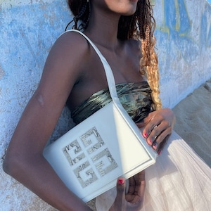 Op de afbeelding: Een witte leren handtas met een slangenhuidpatroon op de voorste klep. De tas heeft een enkele band en een zilveren sluiting.