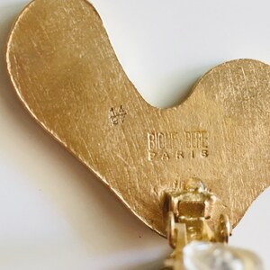 May include: Gold-tone metal earrings with a unique, abstract shape. The back of the earrings feature a clasp closure and the inscription "Biche Pere Paris 14 CT".
