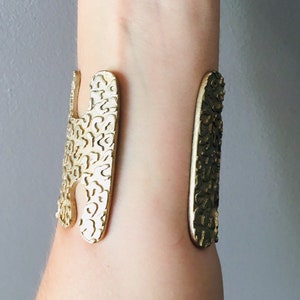 May include: Gold-toned metal cuff bracelet with a textured, abstract design. The bracelet is open and adjustable.