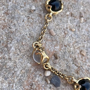 Peut inclure: Bracelet en chaîne dorée avec des perles en verre noir et transparent. Les perles sont serties dans du métal doré et présentent un design délicat.