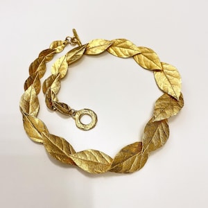 Può includere: Una collana d'oro realizzata con forme di foglie collegate. La collana è un pezzo di grande impatto e sarebbe un'ottima aggiunta a qualsiasi collezione di gioielli.