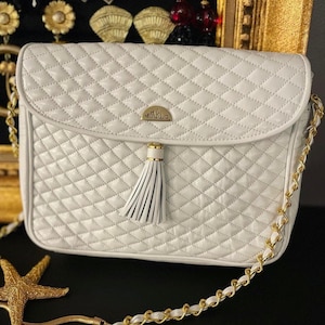 May include: A white quilted shoulder bag with a gold chain strap and a tassel. The bag has a gold logo that says "WARLO".