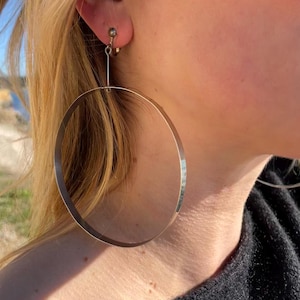 May include: Silver hoop earrings with a clip-on fastening. The earrings are large and circular.