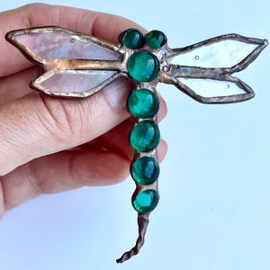 May include: A stained glass dragonfly with a white and iridescent body and a long tail of green glass beads.