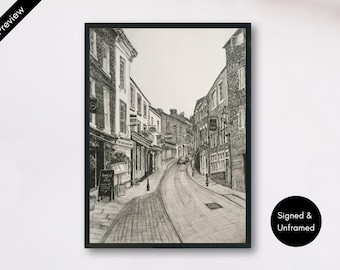May include: A black and white ink drawing of a narrow, sloped cobblestone street lined with multi-storey brick buildings. The perspective shows storefronts on the left and right, with a road curving upwards into the distance under a clear sky.