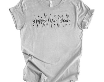 Op de afbeelding: Lichtgrijs t-shirt met de tekst "Happy New Year" in zwart script. De tekst is omgeven door kleine sterrenpatronen. Het shirt is gemaakt van zacht materiaal en heeft korte mouwen.