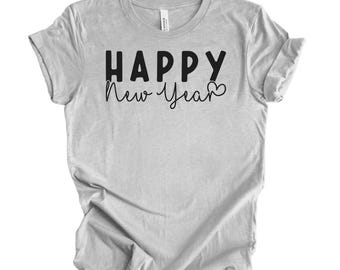 Op de afbeelding: Een lichtgrijs t-shirt met de zwarte tekst "HAPPY New Year". Het woord "HAPPY" is vetgedrukt, terwijl "New Year" in een cursief schrift staat. Twee kleine hartjes staan naast het woord "Year".