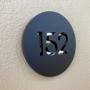 Op de afbeelding: Een zwart rond bord met het nummer 152 uitgesneden uit het midden.