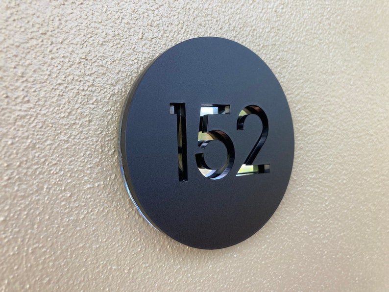 Op de afbeelding: Een zwart rond bord met het nummer 152 uitgesneden uit het midden.