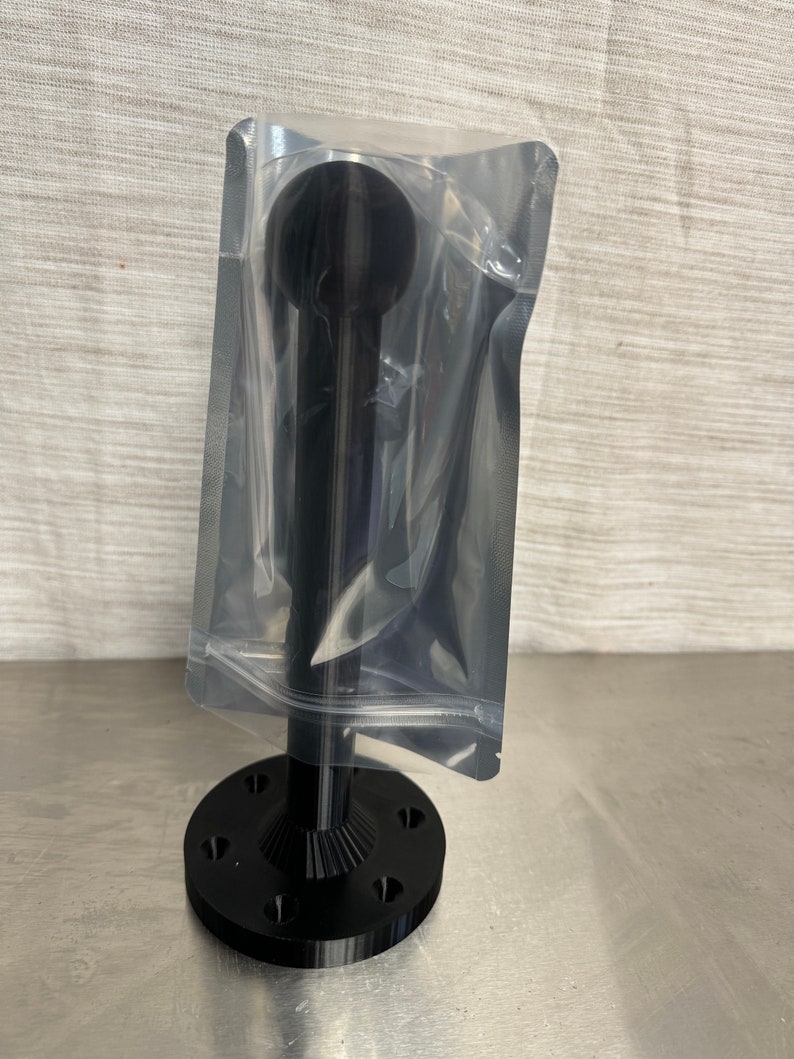 May include: Black metal base with a black metal rod and a black ball on top. The base has a circular shape with a textured surface. The rod is smooth and cylindrical. The ball is smooth and spherical. The base is attached to the rod with a threaded connection. The rod is attached to the ball with a threaded connection. The base has a diameter of approximately 7.6 cm. The rod is approximately 15.2 cm long. The ball is approximately 2.5 cm in diameter.