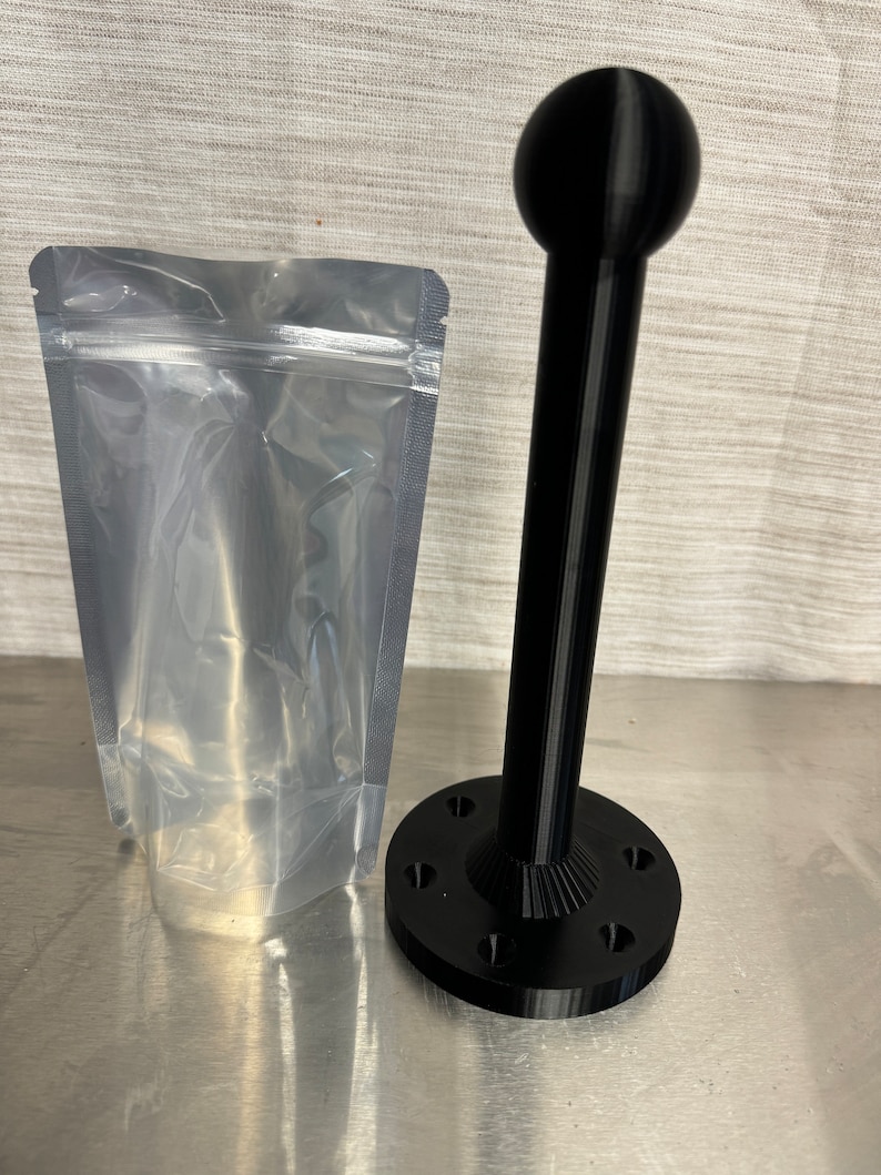 May include: A black plastic 3D printed stand with a round top and a base with six holes. The stand is packaged in a clear plastic bag.