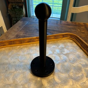 May include: A black metal stand with a round top and a base with six holes. The stand is on a light brown surface with a white pattern.