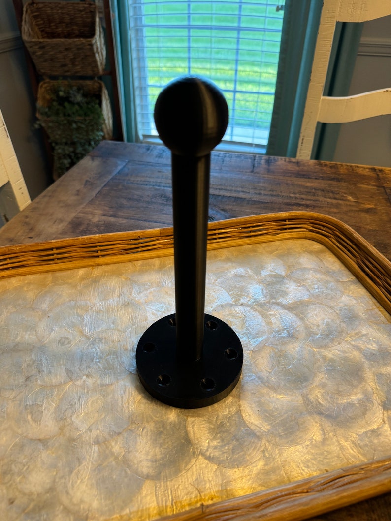 May include: A black metal stand with a round top and a base with six holes. The stand is on a light brown surface with a white pattern.