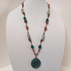 May include: A brown leather necklace with green and white beads and a turquoise pendant with a circular design.