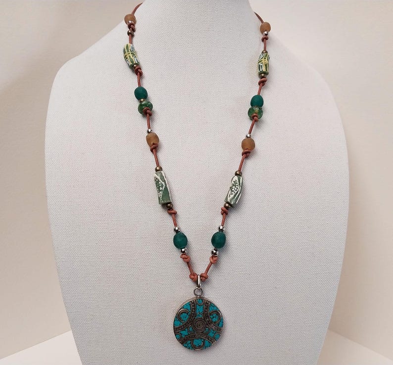 May include: A brown leather necklace with green and white beads and a turquoise pendant with a circular design.