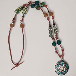 May include: A brown leather necklace with green and brown beads and a turquoise pendant with silver accents.