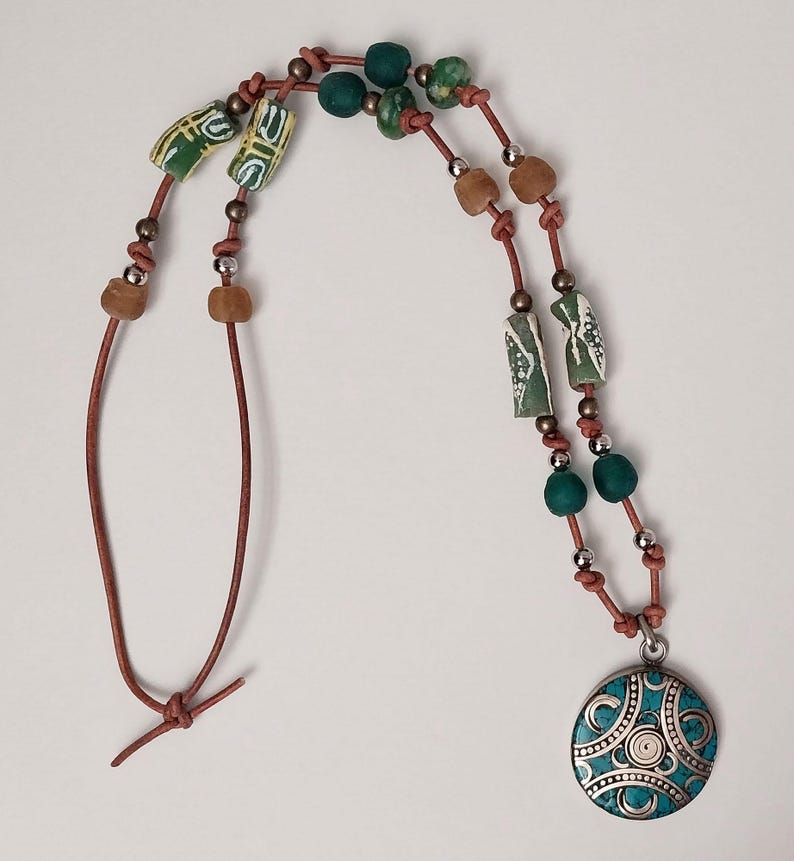 May include: A brown leather necklace with green and brown beads and a turquoise pendant with silver accents.