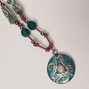 May include: A turquoise and silver pendant necklace with a leather cord. The pendant features a circular design with intricate silver details and a turquoise inlay.