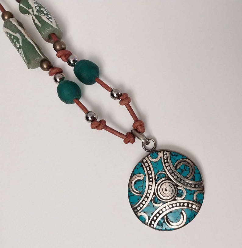 May include: A turquoise and silver pendant necklace with a leather cord. The pendant features a circular design with intricate silver details and a turquoise inlay.