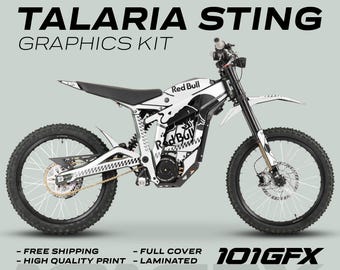 May include: A white and black Talaria Sting electric dirt bike with Red Bull graphics. The bike has a black frame, white wheels, and a black seat. The graphics are printed on the side panels and the front fender. The bike is on a white background.
