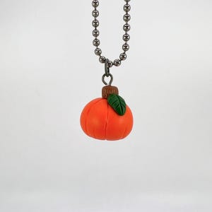 May include: A silver chain necklace with a small orange pumpkin charm. The pumpkin has a green leaf and a brown stem.