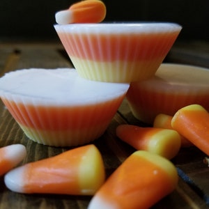 May include: A stack of three white, yellow, and orange candy-themed wax melts, with several orange and yellow candy corn pieces scattered around them.