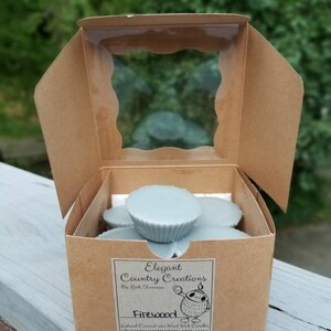 May include: A brown cardboard box with a clear plastic window, containing a stack of light blue wax melts. The box has a label that reads "Elegant Country Creations" and "Firewood".